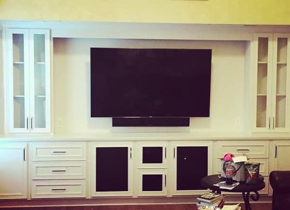 Completed full-wall built-in with white painted cabinets, glass-door uppers, and center TV niche