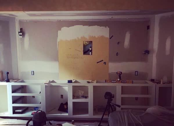 Living room wall with cabinet carcasses framed and primed, wall partially patched around TV niche