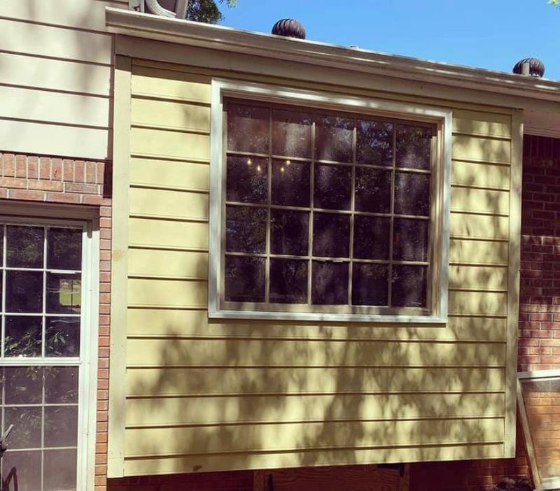 Completed exterior with new lap siding, large picture window, and white casing trim