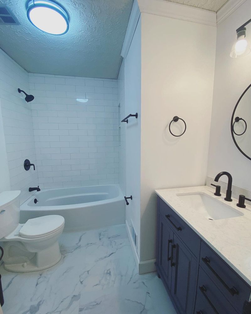 Renovated bathroom with navy blue vanity, white quartz top, marble-look tile floor, and subway tile shower