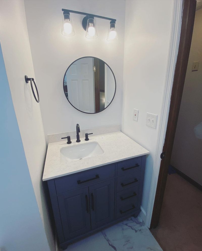 Updated vanity area with round black-framed mirror, industrial light fixture, and matte black faucet