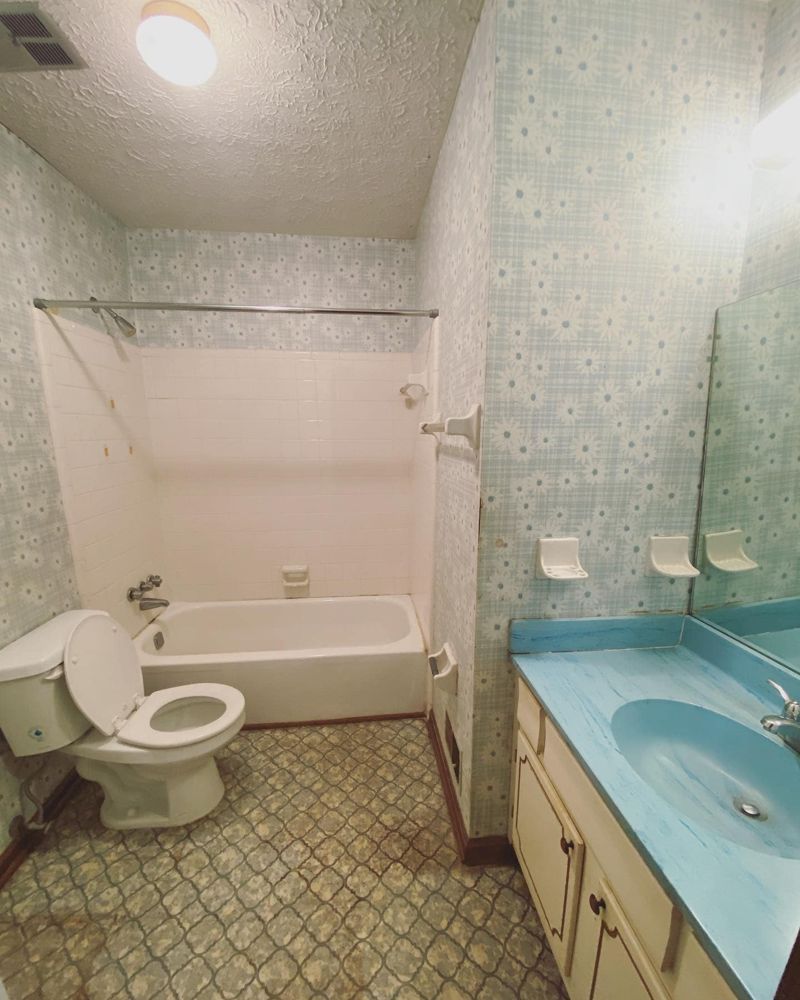 Dated 1970s bathroom with daisy wallpaper, blue laminate countertop, and patterned vinyl floor
