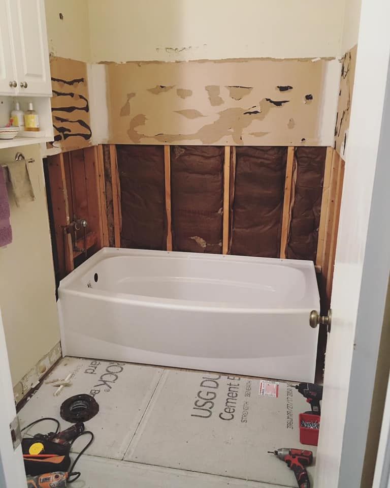 Bathroom demo in progress — tile removed to studs, cement board on floor, tub exposed