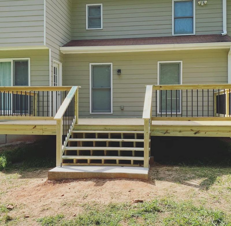 Full-width pressure-treated deck with centered stairs and black iron balusters