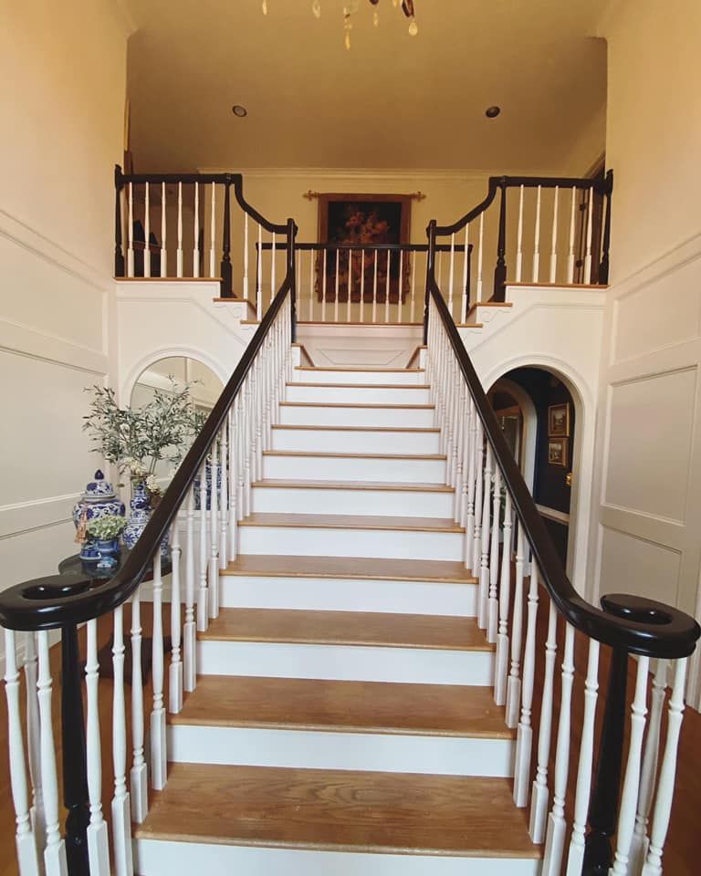 Grand foyer staircase with dark-stained curved handrails, white turned balusters, and oak treads