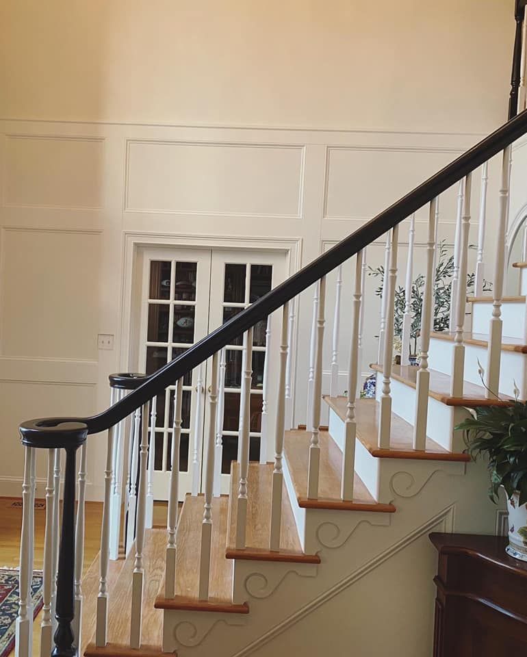 Dark-stained curved handrail with white turned balusters and wainscoting paneling in two-story foyer