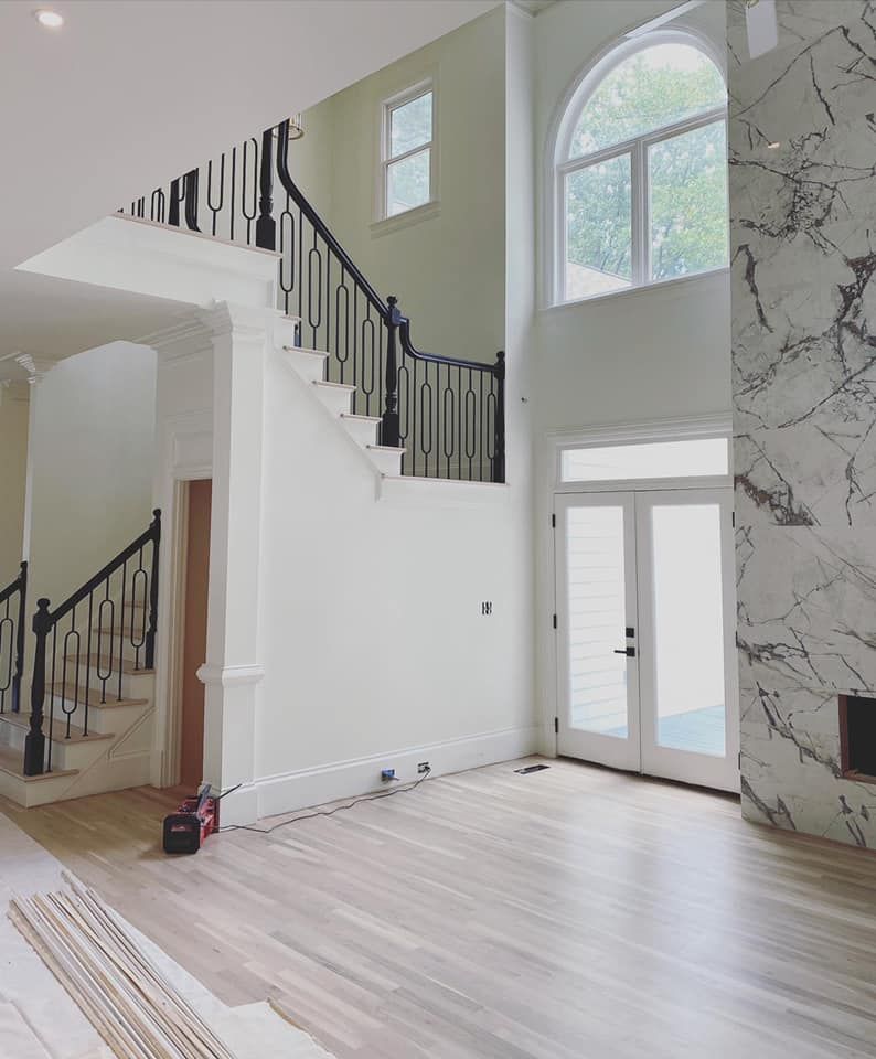Two-story foyer with matte black curved handrail, bold loop iron balusters, and wainscoting stair wall