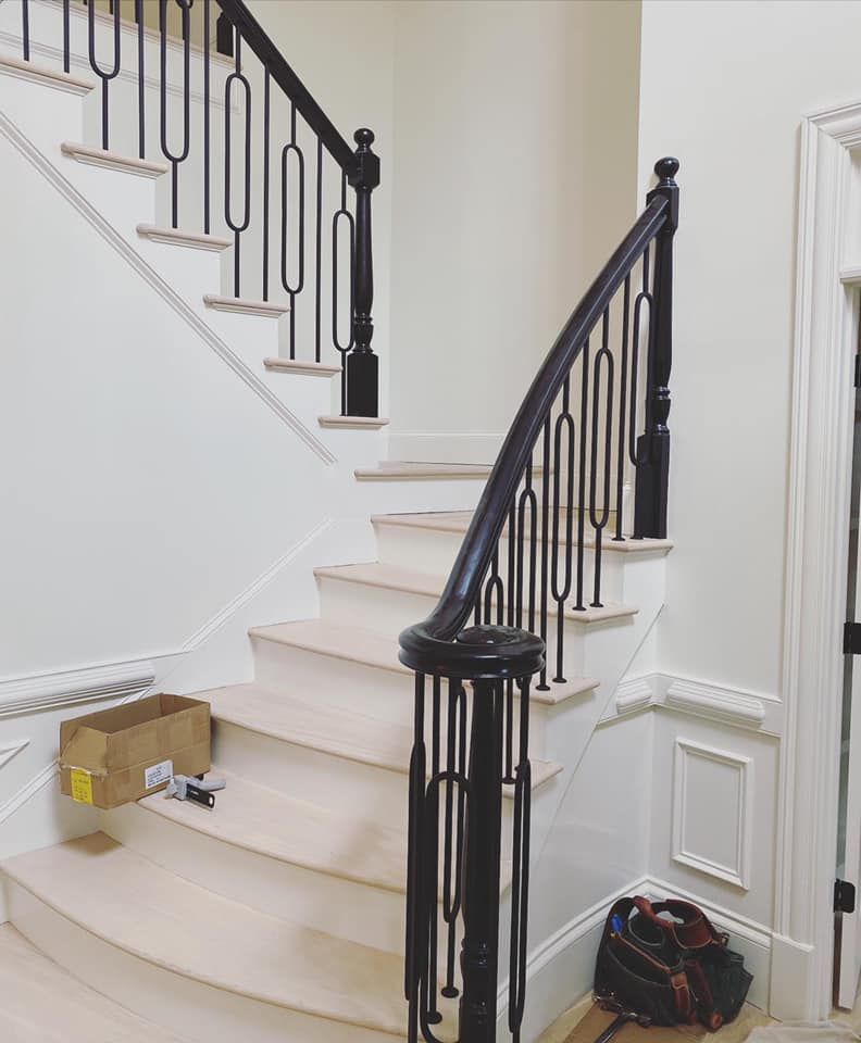 Curved black handrail wrapping newel post with loop-style iron balusters and painted wainscoting