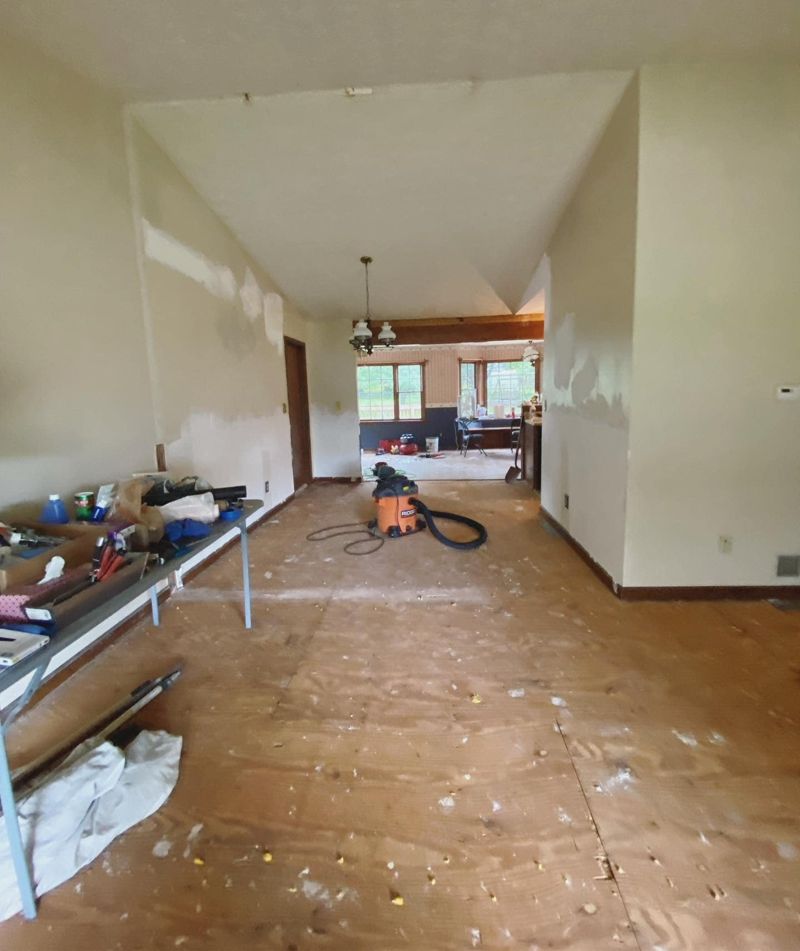Living area mid-demolition with exposed subfloor and patched walls
