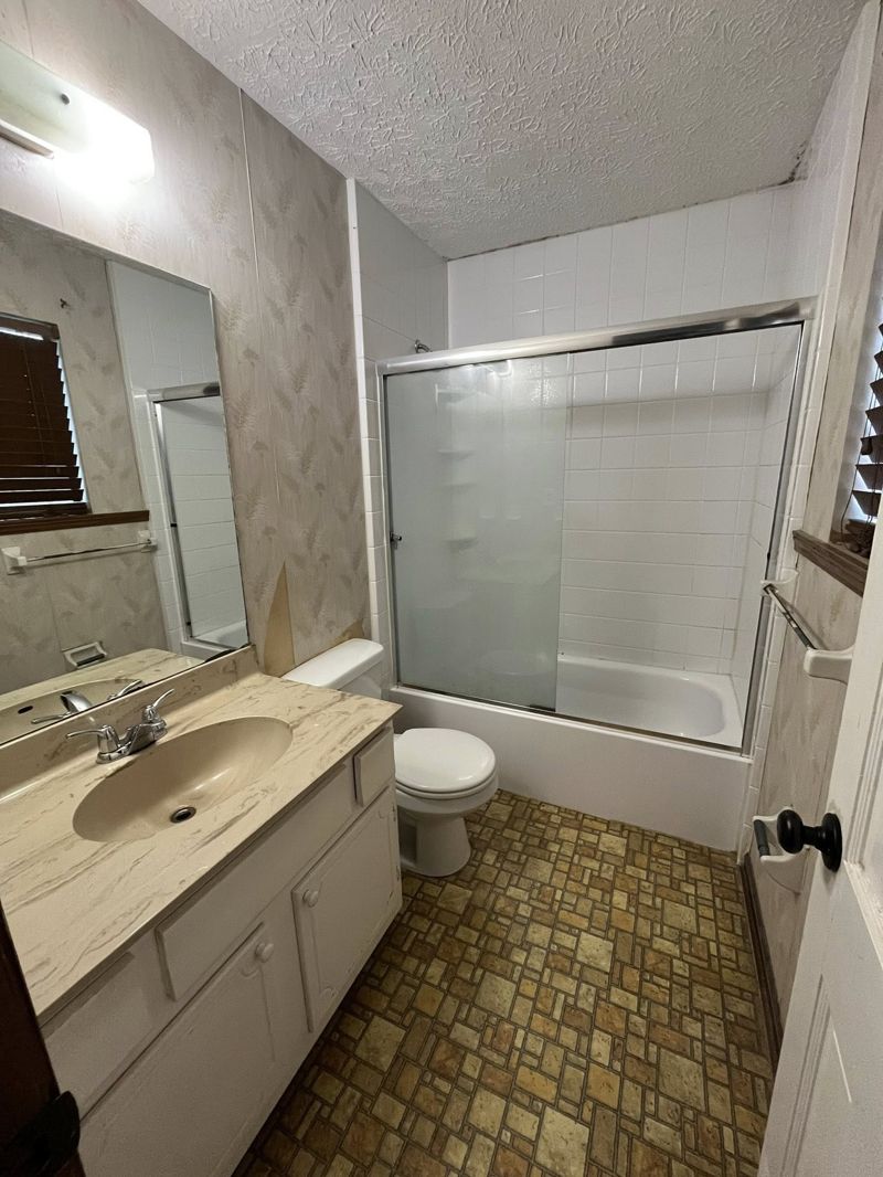 Dated bathroom with wallpaper, cultured marble vanity, and frosted sliding tub doors