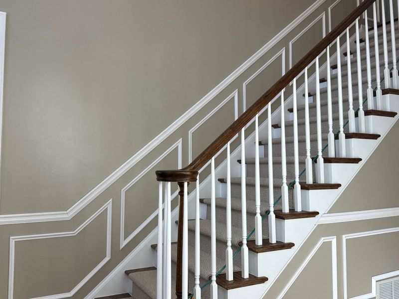 Picture frame wainscoting along staircase wall with stained oak handrail