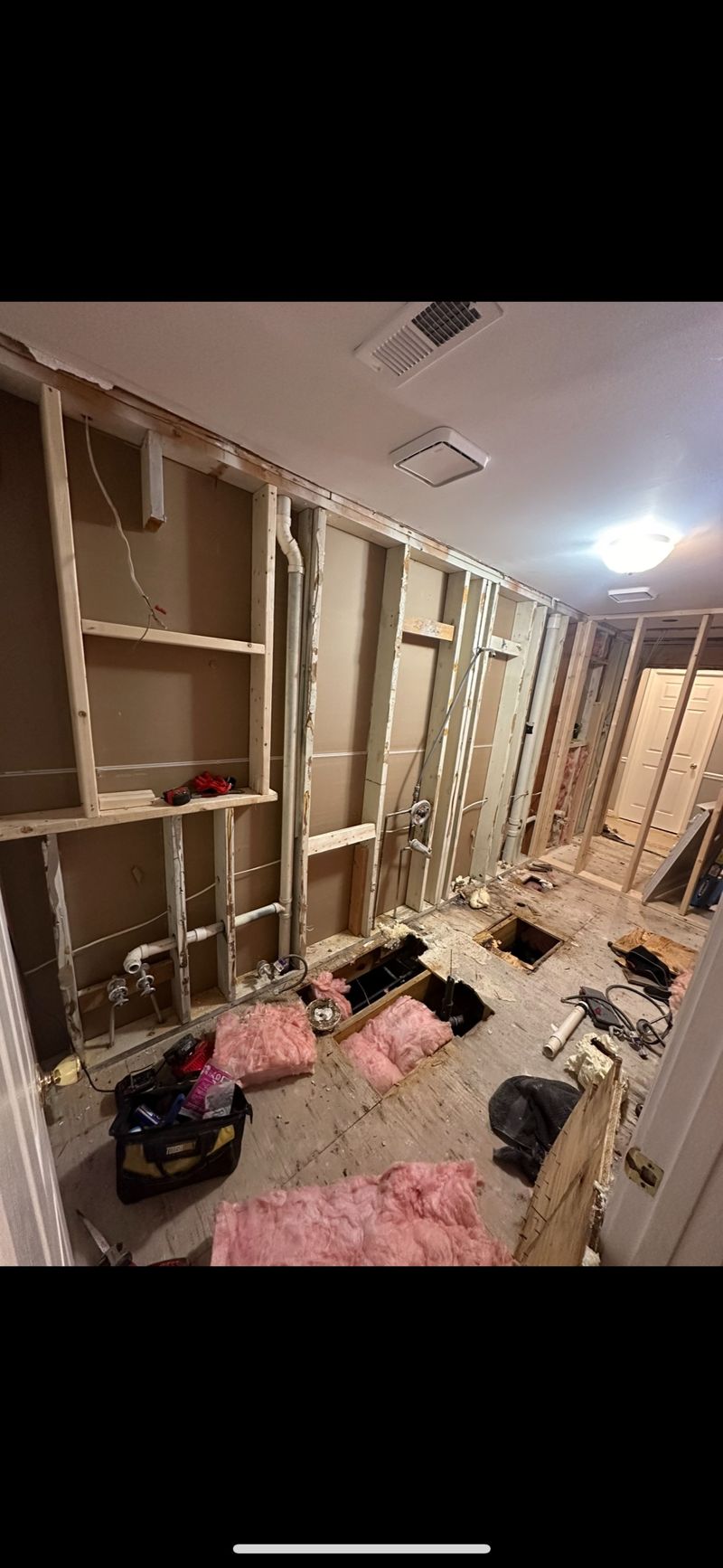 Bathroom demo in progress with bare framing and subfloor opened for plumbing rough-in