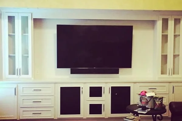 Completed full-wall built-in with white painted cabinets, glass-door uppers, and center TV niche