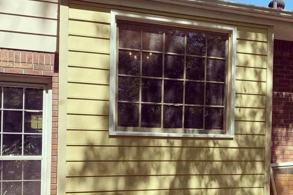 Completed exterior with new lap siding, large picture window, and white casing trim