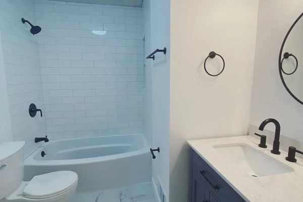 Renovated bathroom with navy blue vanity, white quartz top, marble-look tile floor, and subway tile shower