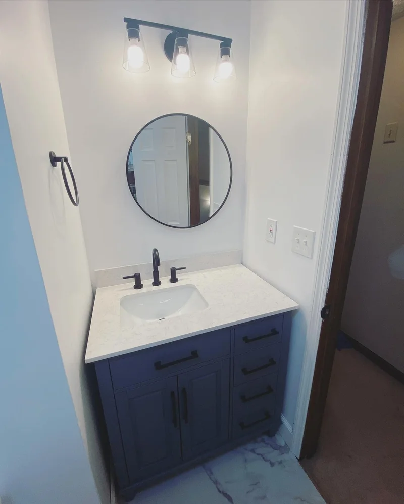 Updated vanity area with round black-framed mirror, industrial light fixture, and matte black faucet