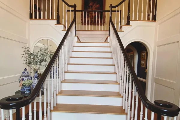 Grand foyer staircase with dark-stained curved handrails, white turned balusters, and oak treads