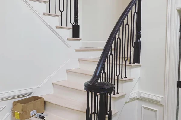Curved black handrail wrapping newel post with loop-style iron balusters and painted wainscoting