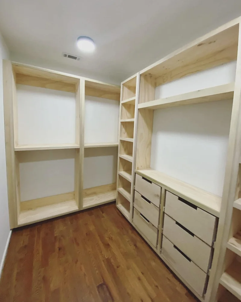 Built-in drawers with routed finger pulls alongside open hanging bays and center shelving unit