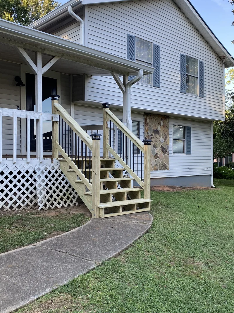Rebuilt front porch steps with handrails, black iron balusters, and post caps meeting the walkway