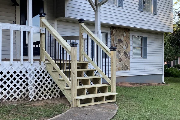 Rebuilt front porch steps with handrails, black iron balusters, and post caps meeting the walkway