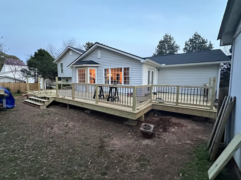 Rebuilt deck with railing and stair run wrapping the back of the house at dusk
