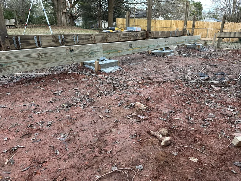 Timber retaining wall on concrete footings going up along the regraded backyard