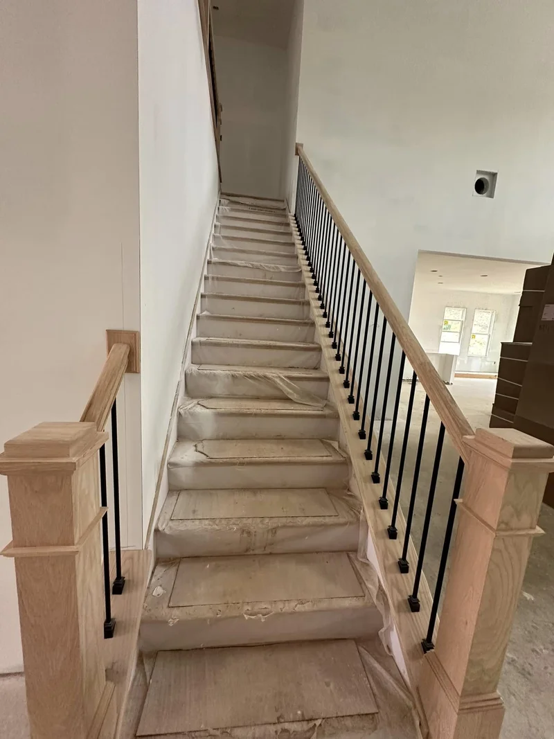 Staircase under construction with protected treads and baluster installation