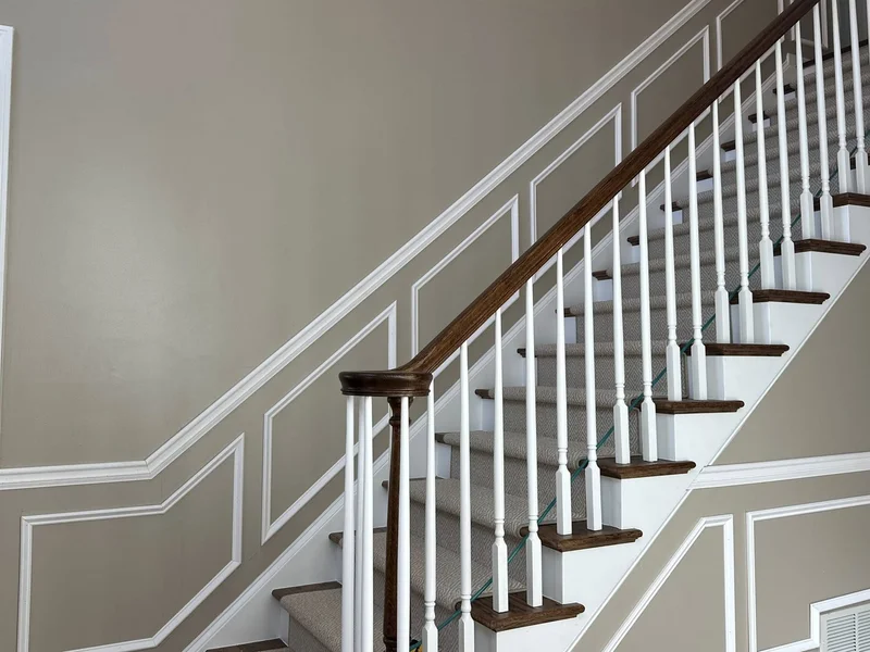 Picture frame wainscoting along staircase wall with stained oak handrail