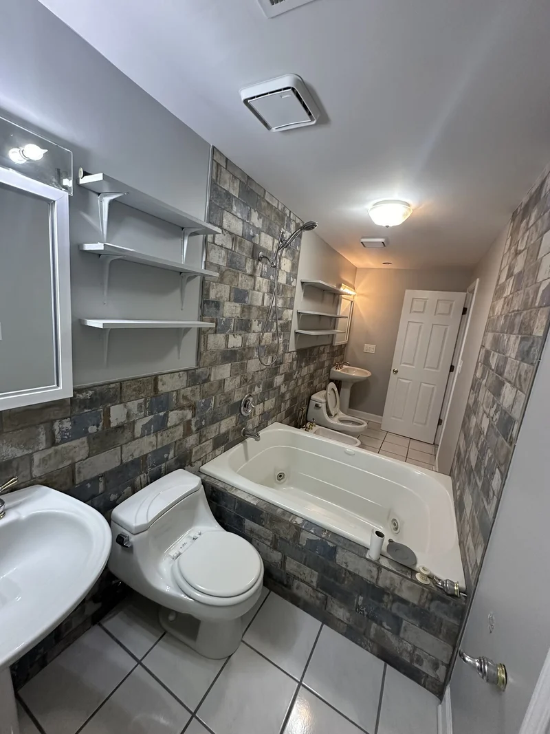 Dated bathroom with distressed brick-look wall tile, jetted tub, and unconventional dual-commode layout