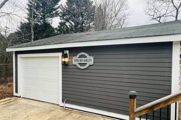 Renovated garage with dark gray lap siding, white trim, new garage door, and wall lantern