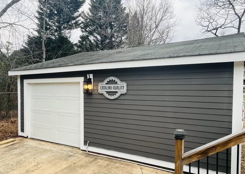 Renovated garage with dark gray lap siding, white trim, new garage door, and wall lantern