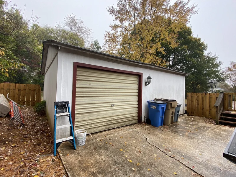 Garage before renovation with worn white paint and an aging roll-up door